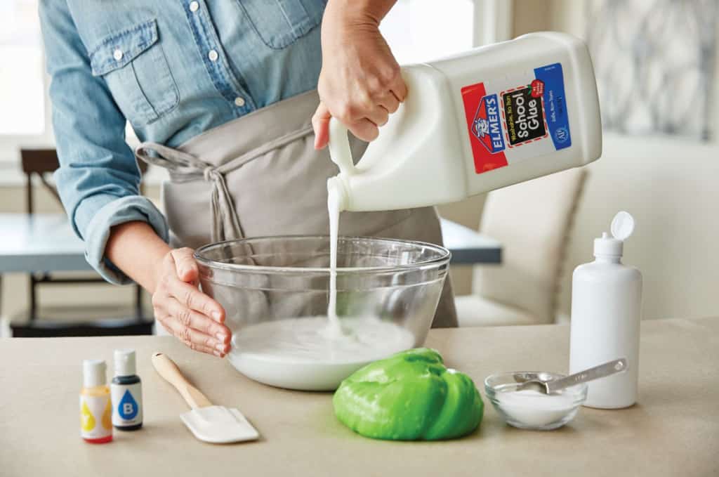 Pouring elmer's white school glue into a kitchen bowl as the first step in making slime recipe